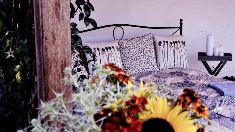 Gemütliches Bett mit dekorativen Kissen und Blumen im Vordergrund.