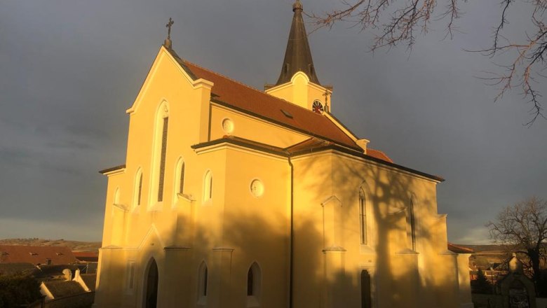Gelbe Kirche in Glaubendorf im Sonnenlicht mit dunklem Himmel.