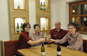 Vier Personen stoßen mit Weingläsern an einem Tisch an.