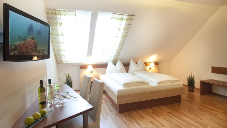 Gästezimmer, © Astrid Bartl Ein gemütliches Gästezimmer mit Doppelbett, Flachbildfernseher, Tisch mit Stühlen und Dachfenstern.