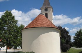 Ortskapelle Hl. Barbara mit rundem Dach und Turm vor blauem Himmel.