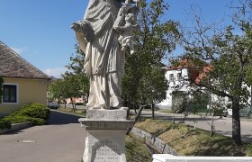 Statue des Heiligen Johannes Nepomuk in Obermarkersdorf, umgeben von Bäumen und Gebäuden.