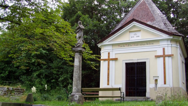 Kapelle mit Statue und Kreuz in einem grünen Park.