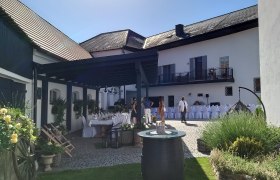 Innenhof mit gedeckten Tischen, Blumen und Personen bei sonnigem Wetter.