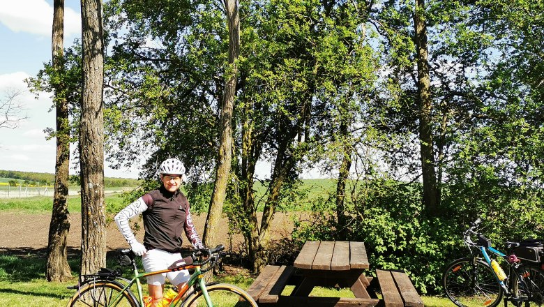 Person mit Fahrrad neben Picknicktisch im Grünen.