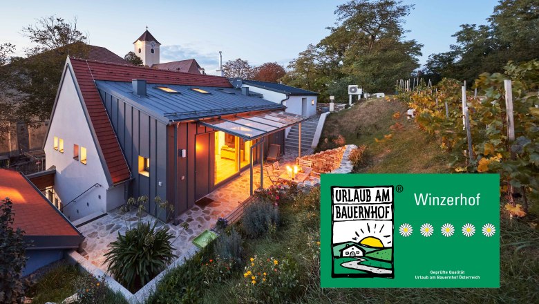 Weinviertler Kellerstöckl, © Andreas Hofer Ein modernes Kellerstöckl im Weinviertel bei Dämmerung, umgeben von Weinreben und einem Garten. Ein Schild zeigt 'Urlaub am Bauernhof'.