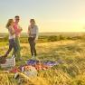 Drei Personen beim Picknick auf einer Wiese bei Sonnenuntergang.