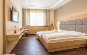 Modernes Gästezimmer mit Doppelbett, Flachbildfernseher und Holzmöbeln.