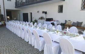 Langer, festlich gedeckter Tisch im Freien mit wei&szlig;en Tischdecken und Stuhlhussen.