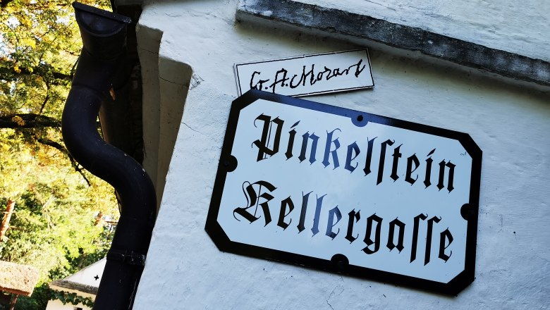 Schild mit der Aufschrift 'Pinkelstein Kellergasse' an einer wei&szlig;en Wand.