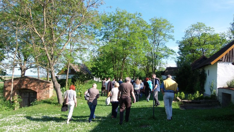 Gruppe von Menschen geht durch eine grüne Landschaft mit Bäumen und alten Gebäuden.