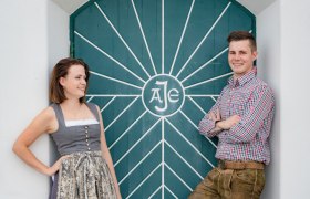 Ein Mann und eine Frau in traditioneller Kleidung vor einer grünen Tür mit geometrischem Muster.