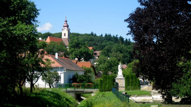 Landschaft mit Kirche und Statue in einem Dorf.