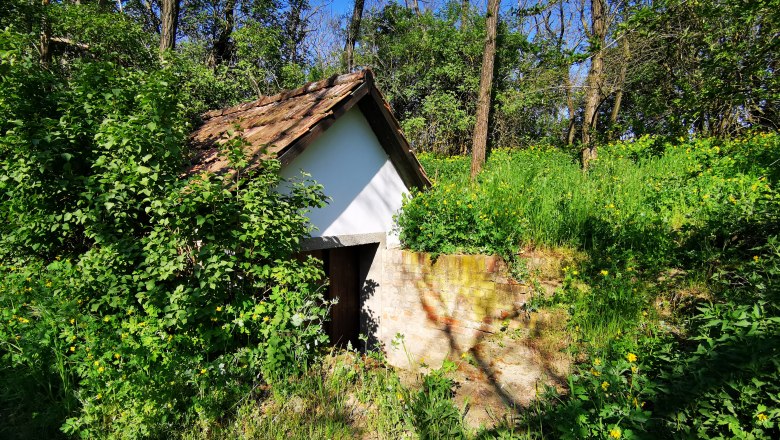 Kleines Häuschen mit Ziegeldach, umgeben von üppigem Grün und Bäumen.