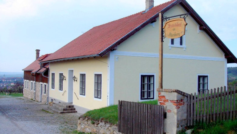 Winzerhaus mit gelber Fassade und rotem Dach in ländlicher Umgebung.