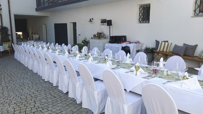 Langer, festlich gedeckter Tisch im Freien mit wei&szlig;en Tischdecken und Stuhlhussen.