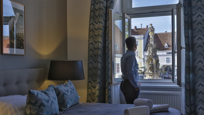 Person steht am Fenster eines Hotelzimmers und blickt auf einen Brunnen draußen.