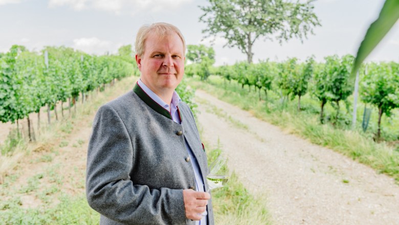 Mann in traditioneller Kleidung mit Weinglas in einem Weinberg.