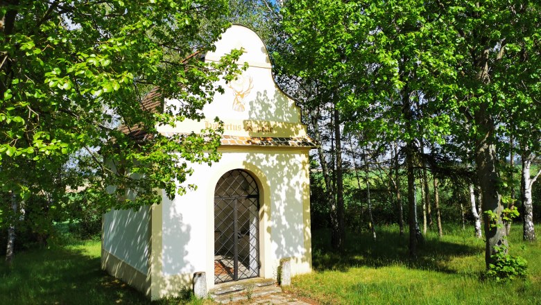 Kleine Kapelle umgeben von Bäumen im Grünen.