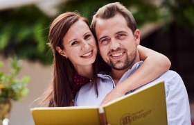 Ein lächelndes Paar hält eine Menükarte beim Heurigen Burger.