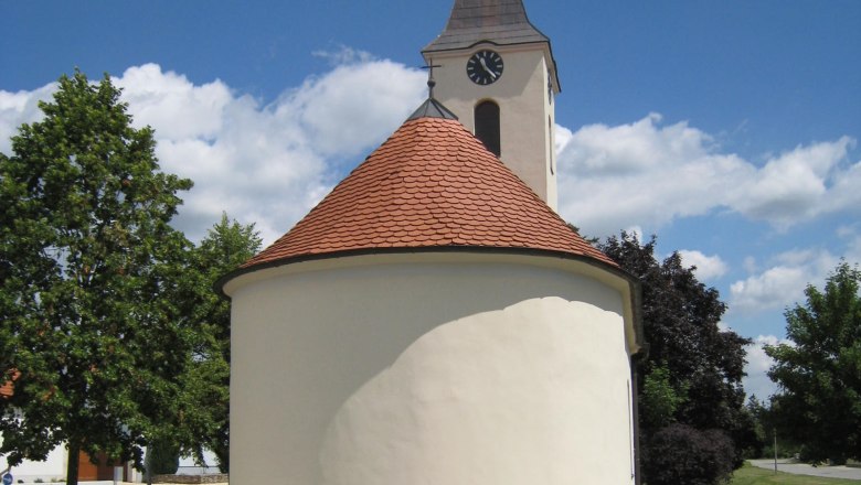 Ortskapelle Hl. Barbara mit rundem Dach und Turm vor blauem Himmel.