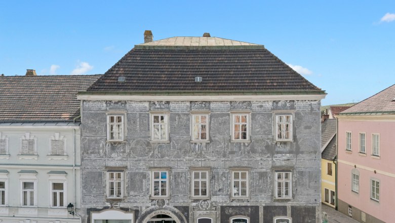 Historisches Gebäude mit grauer Fassade und dekorativen Malereien in einer Stadt.