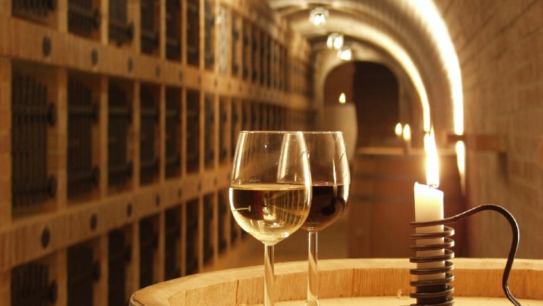 Zwei Weingläser und eine Kerze auf einem Fass in einem Weinkeller.