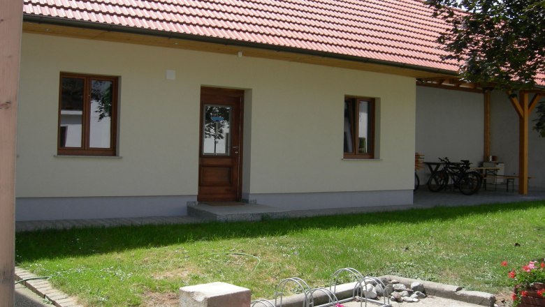 Innenhof, © Hörker Ein Innenhof mit einem Gebäude mit rotem Ziegeldach, Holztür und Fenstern. Im Vordergrund sind Blumen und ein Fahrradständer zu sehen.