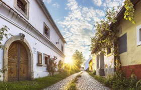 Kopfsteinpflasterstra&szlig;e in R&ouml;schitz mit traditionellen Geb&auml;uden und Sonnenuntergang im Hintergrund.