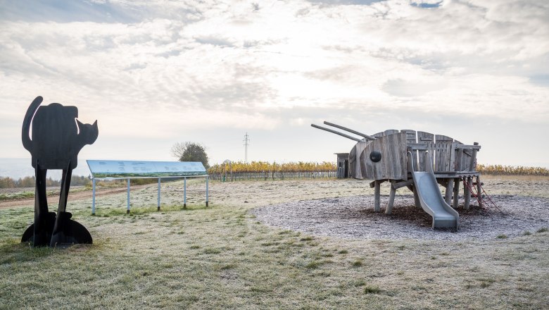 Spielplatz mit Holzspielgerät in Form eines Tieres und Katzenskulptur.