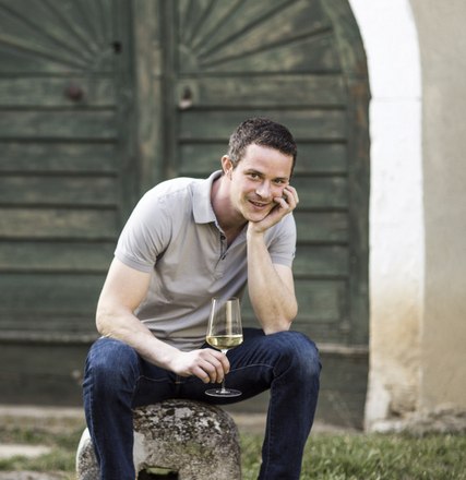 Ein Mann sitzt l&auml;chelnd mit einem Weinglas in der Hand vor einer alten Holzt&uuml;r.