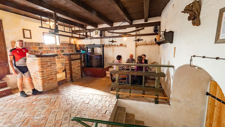 Gem&uuml;tlicher Weinkeller mit Personen an einem Tisch und einem Mann in Radkleidung.