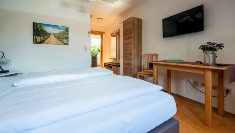 Gemütliches Hotelzimmer mit Doppelbett, Holzmöbeln, TV und Pflanzen.