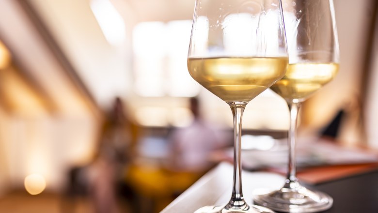 Zwei Weingläser mit Weißwein auf einem Tisch, unscharfer Hintergrund.