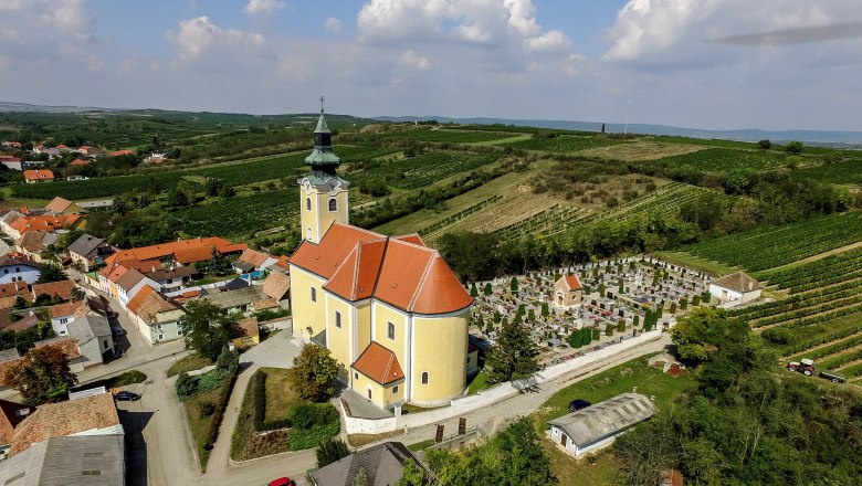 Luftaufnahme der Pfarrkirche in Röschitz mit umliegendem Friedhof und Weinbergen.
