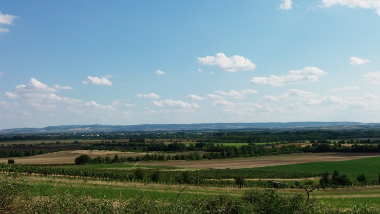 Weite Landschaft mit Feldern und Hügeln unter blauem Himmel mit Wolken.