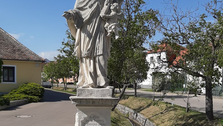 Statue des Heiligen Johannes Nepomuk in Obermarkersdorf, umgeben von Bäumen und Gebäuden.