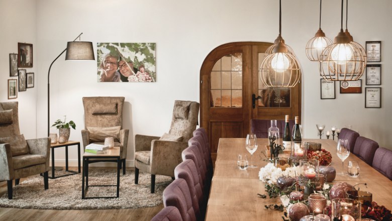 Gem&uuml;tlicher Verkostungsraum mit Tisch, St&uuml;hlen, Sesseln und Dekoration.