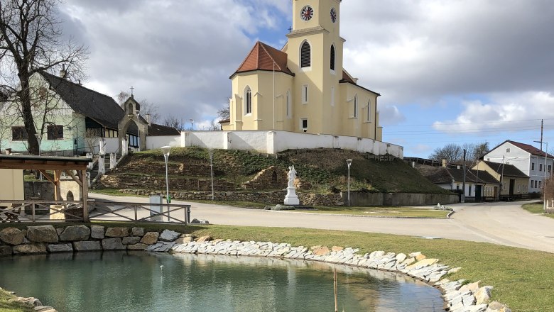 Kirche in Glaubendorf mit Teich im Vordergrund.