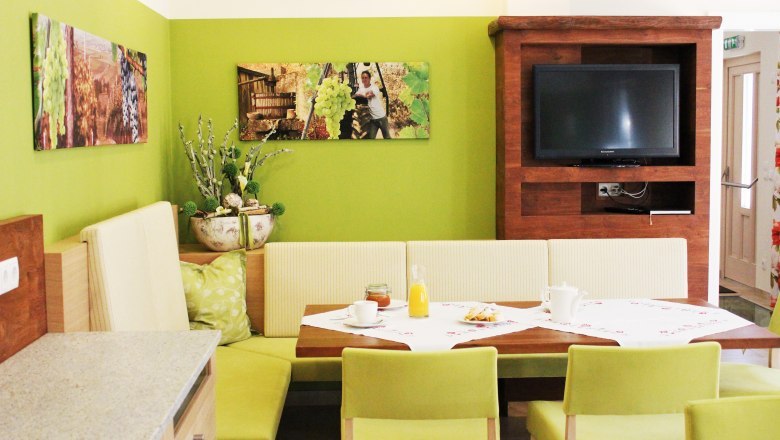 Gästehaus Loiskandl, © Gästehaus Loiskandl / Elisabeth Widhalm Gemütlicher Essbereich mit grünen Wänden, Holzmöbeln und einem Fernseher.
