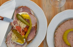 Zwei Teller mit belegten Broten und zwei Gläser Weißwein auf einem Holztisch.