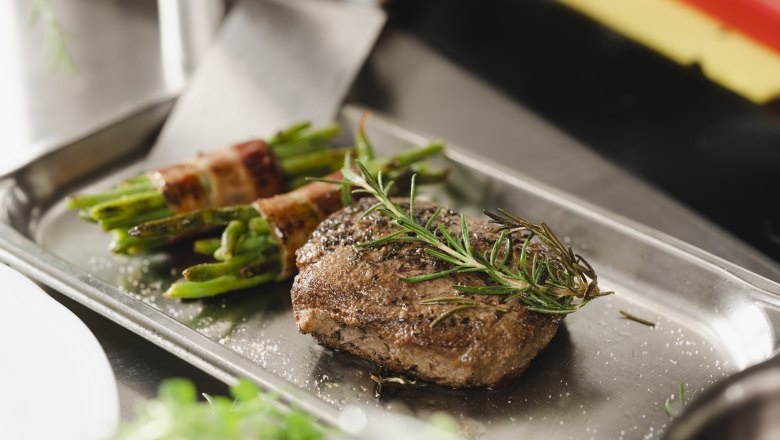 Ein Steak mit Rosmarin und Bohnen im Speckmantel auf einem Metalltablett.
