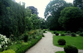 Ein gepflegter Gartenweg im Schlosspark Mühlbach, umgeben von Büschen und Bäumen.