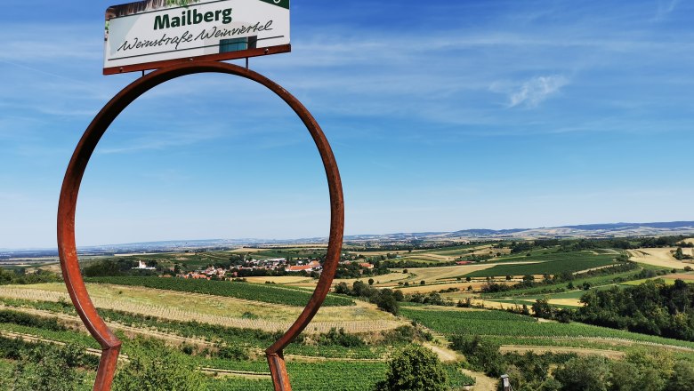 Landschaft mit Weinbergen und einem Schild mit der Aufschrift 'Mailberg Weinstraße Weinviertel'.
