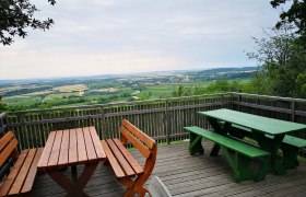 Aussichtsplattform mit Holzbänken und Tischen, Blick auf weite Landschaft und Felder.