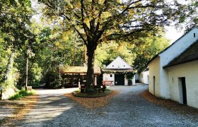 Idyllischer Platz in Raschala mit Kopfsteinpflaster, Bäumen und weißen Gebäuden.