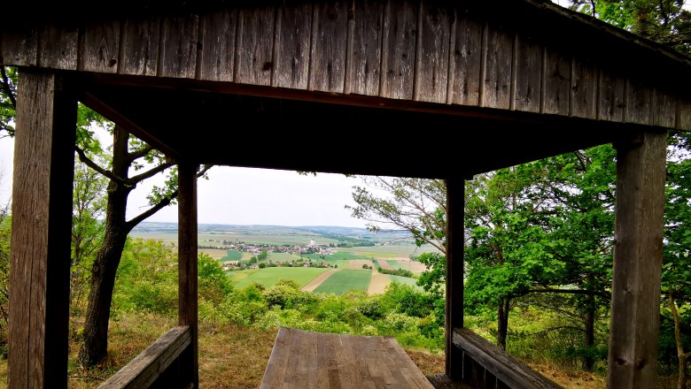 Holzhütte mit Blick auf Felder und Dorf in der Ferne.