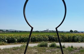 Metallrahmen in Form eines Schlüssellochs mit Blick auf Wullersdorf und Sonnenblumenfeld.
