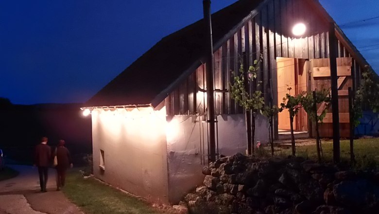 Beleuchtetes Weinkellergebäude bei Nacht mit zwei Personen auf einem Weg.