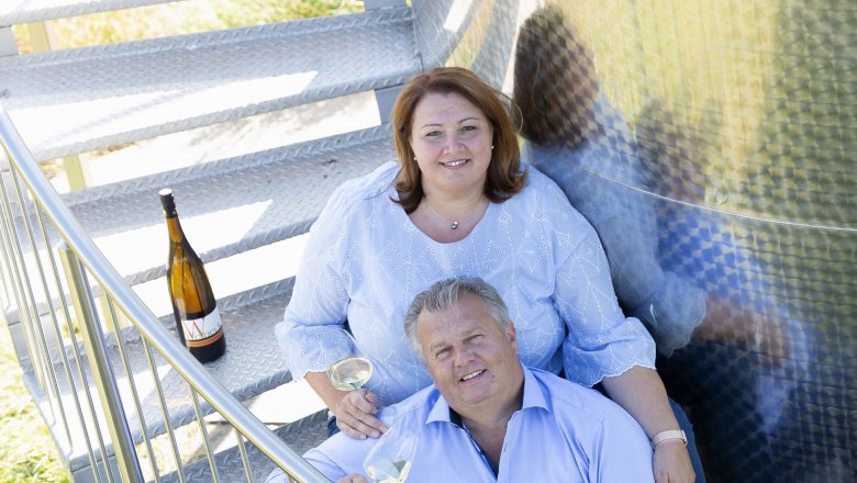Ein Mann und eine Frau sitzen auf einer Metalltreppe mit Weingläsern in der Hand.